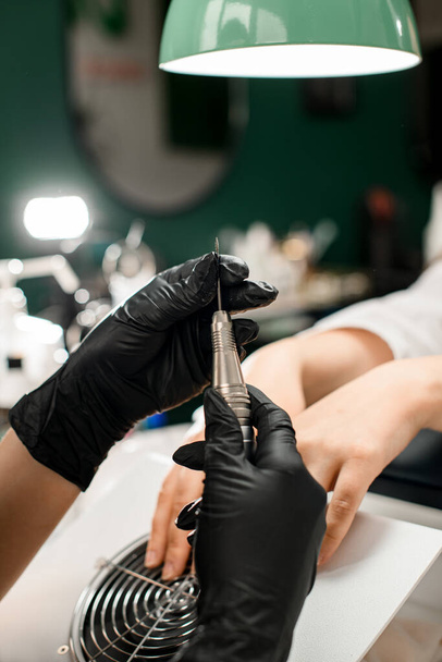 Close-up of female hands of manicure master in black rubber gloves with cuticle remover device in a beauty salon. Professional manicure tool. - Valokuva, kuva
