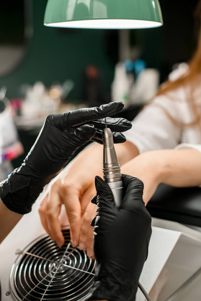 Female hands of manicure master in black rubber gloves with cuticle remover device in a beauty salon. Professional manicure tool. - Foto, Imagem