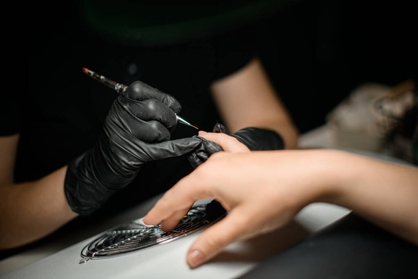 Close-up view of manicurist hands masterfully applies manicure nail paint with thin brush. Beautician salon. Manicure nails polish procedure. - Fotó, kép