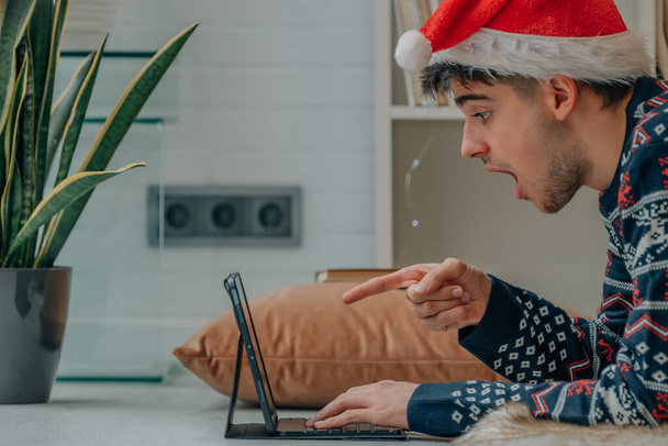 mladý muž na vánoce doma s počítačem a výrazem překvapení - Fotografie, Obrázek