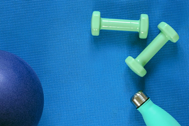 Top view of ball, dumbbells and bottle with water on blue sports mat. Flat lay, copy space. Home training concept. - Photo, Image