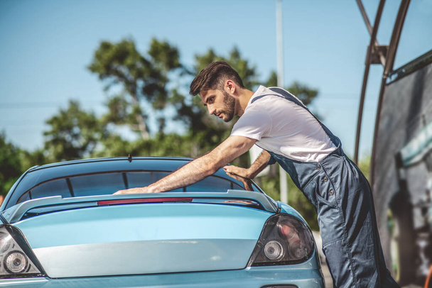 Serious concentrated young professional car service worker dressed in the uniform washing the exterior of a client vehicle outdoors - Фото, изображение