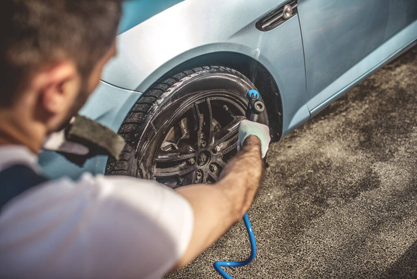 Вид ззаду професійного автовиконавця, який чистить брудний фланцевий автомобіль та шину за допомогою мийки під тиском
 - Фото, зображення
