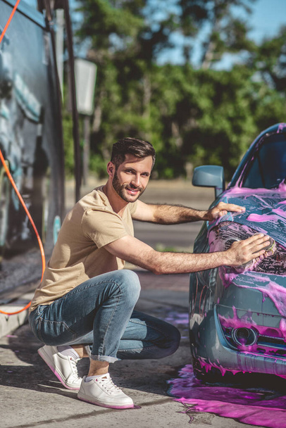 笑顔の喜び若い白人自動車サービスの労働者マイクロファイバースポンジで車のヘッドランプを拭く - 写真・画像
