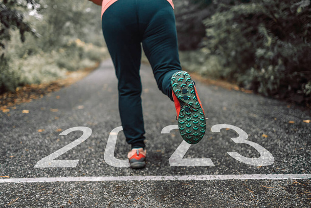 Numbers 2023 written on the road towards new goals in 2023 and female runners are starting to run. New Year 2023 with new ambitions, challenge, plans, goals and visions. High quality photo - Foto, afbeelding