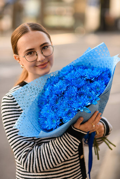 attractive smiling woman holds in her hands large lush bouquet of blue chrysanthemums in wrapping paper - Photo, Image