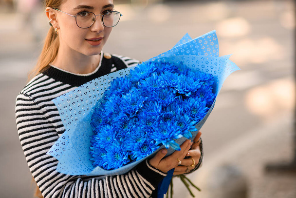 young woman holds in her hands large lush bouquet of blue chrysanthemums in wrapping paper - Foto, Imagem