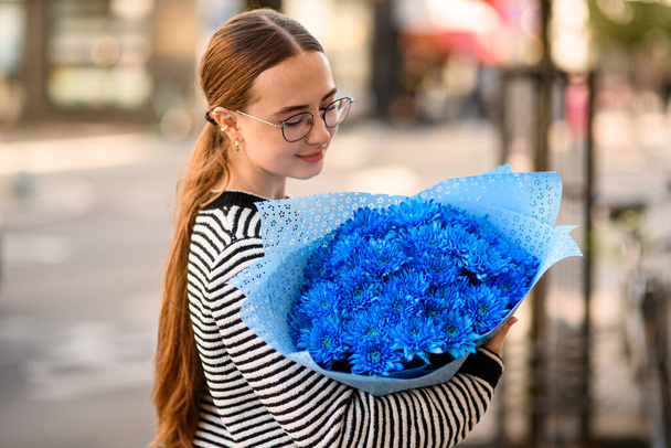 beautiful woman gently holds in her hands large lush bouquet of blue chrysanthemums in wrapping paper and look at it - Photo, image