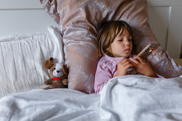 niña enferma tendida en la cama viendo dibujos animados con su juguete favorito - Foto, imagen