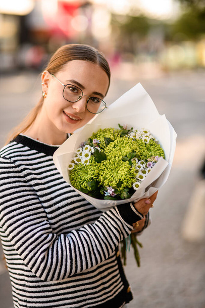 pretty smiling woman holds bouquet of curly green chrysanthemums and small white daisy-like chrysanthemums in wrapping paper in her hands - Photo, image