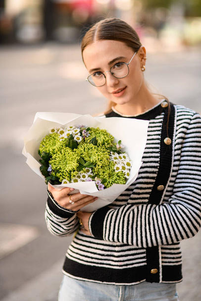 handsome woman holds bouquet of curly green chrysanthemums and small white daisy-like chrysanthemums in wrapping paper in her hands - Fotoğraf, Görsel