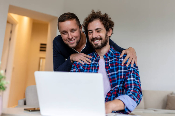 Ihana homopariskunta nauraa yhdessä istuessaan olohuoneessaan kotona. Kaksi romanttinen nuori mies ystäville hauskaa surffata internetissä sisätiloissa. Nuori homo pari asuu yhdessä. - Valokuva, kuva