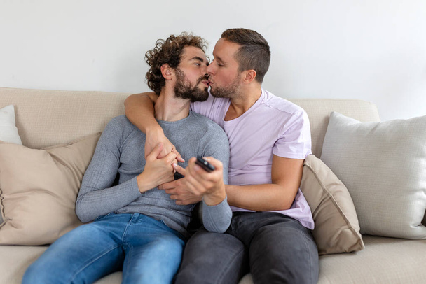 Junges homosexuelles Paar entspannt sich auf Sofa im Wohnzimmer, umarmt und genießt beim Fernsehen - Foto, Bild