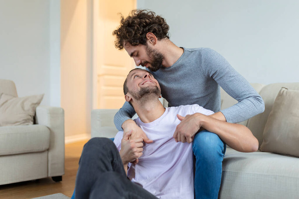 Αγαπώντας το ομοφυλόφιλο ζευγάρι του ίδιου φύλου ξαπλωμένο στον καναπέ στο σπίτι και χαλαρώνοντας, αγκαλιάζοντας μαζί - Φωτογραφία, εικόνα