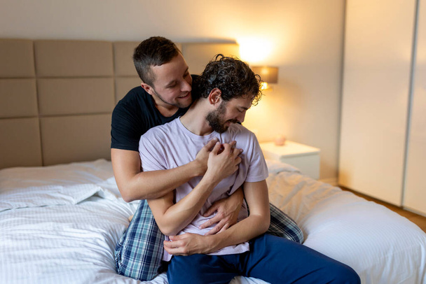 目を閉じてお互いを受け入れるゲイのカップル。2人の若い男性愛好家が朝のベッドで一緒に顔に触れる。愛情若いですゲイカップルボンディングでホーム. - 写真・画像