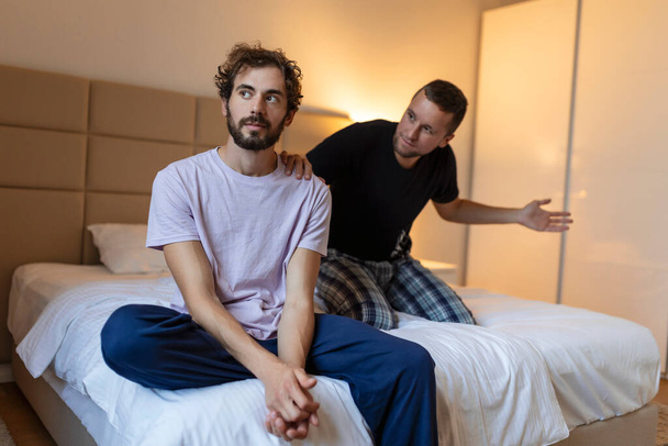 Frustrated sad boyfriend sit on bed think of relationship problems, thoughtful gay couple after quarrel lost in thoughts, upset lovers consider break up, offended person disappointed by boyfriend - Фото, изображение