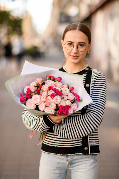 handsome woman gently holds bouquet of bright pink roses in wrapping paper in her hands - Foto, Imagen