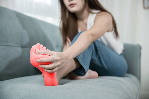 Asian young woman sit on sofa massage her feet and stretch muscles have symptoms feeling pain, beautiful female problems sick illness with foot at home, painful ankle injury, Healthcare and medical - Fotoğraf, Görsel