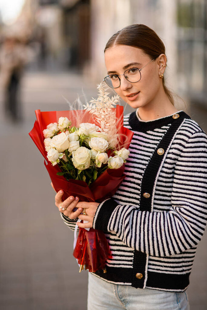 view on pretty woman with bouquet of white roses in red wrapping paper in her hands - Foto, Imagen