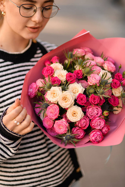 wonderful bouquet with fresh white and pink roses and thistles in wrapping paper in hands of woman - Photo, image