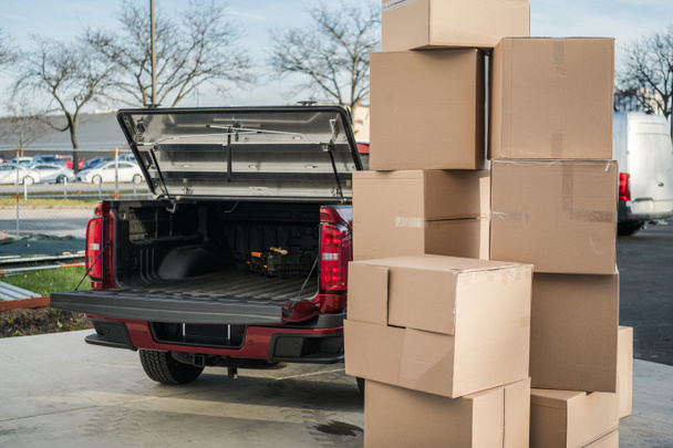 Stack of Cardboard Packages Placed Outside Ready to Be Loaded for Transportation. Pickup Truck with Open Trunk in the Background. Moving Services Theme. - Photo, Image