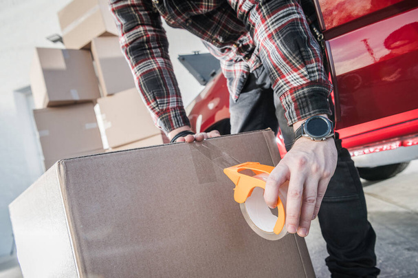 Moving Company Worker Securing Cardboard Box with Transparent Packing Tape for Safe Transportation. Professional Relocation Services. - Photo, Image