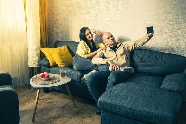 Pár Použijte Smartphone zařízení, Sedět na gauči útulný byt. Vezmi si Selfie jako přítele a přítelkyni. Dělat video chat na internetu, používat sociální média, streaming live video - Fotografie, Obrázek