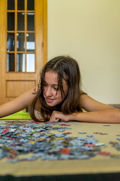 Teenage brunette girl doing puzzle lying on the floor of her house, she spends time running away from technology and enjoying traditional games - Photo, Image