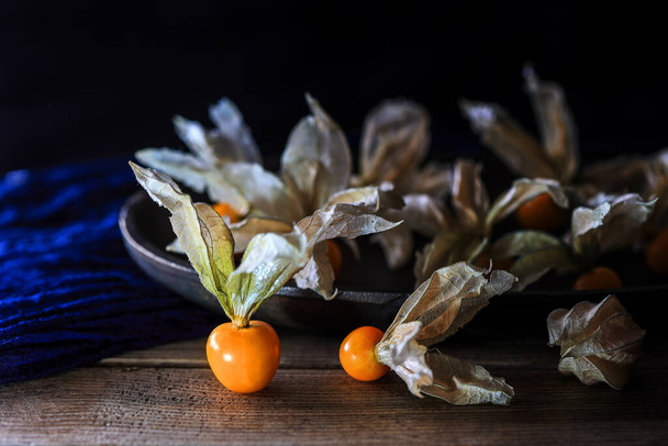 Cape gooseberries - Physalis peruviana, with an old metal plate on table with blue napkin at the dark background and copy space - dark and moody photography - Фото, изображение