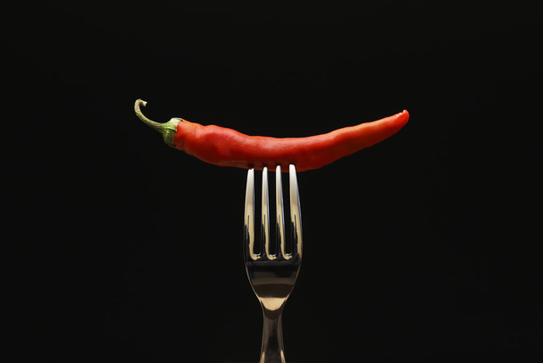 Pimienta roja en un tenedor sobre un fondo negro. Primer plano - Foto, Imagen