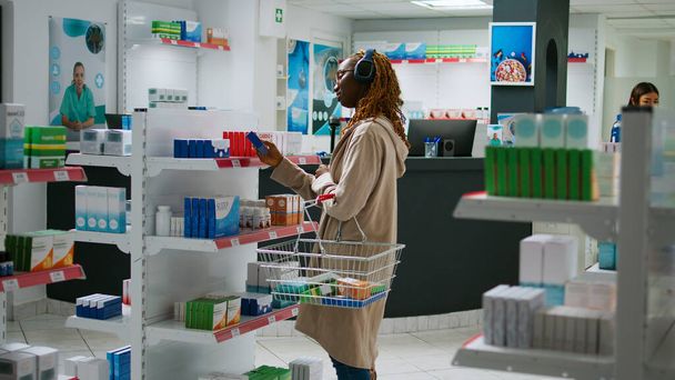 Afrikai amerikai vásárló vizsgálja gyógyszerek polcokon vásárolni vényköteles gyógyszerek és vitaminok gyógyszertár boltban. Ügyfél ül a gyógyszertár pult vásárolni gyógyszeripari termékek. - Fotó, kép