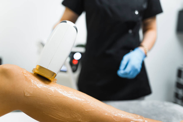 cosmetologist segurando um aparelho de depilação a laser e colocá-lo em uma perna clientes para remover o cabelo, vista close-up. Foto de alta qualidade - Foto, Imagem