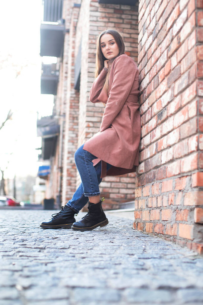 Autumn image of a model, a girl in a coat and boots in the city. Stylish girl near a brick wall - Foto, imagen