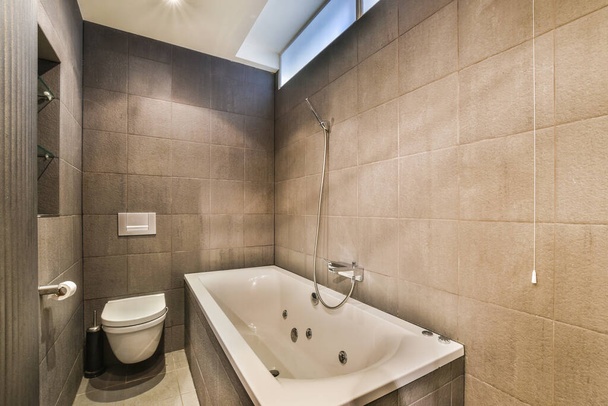 Bañera con ducha de vidrio colocada en esquina cerca del lavabo y espejo en un pequeño cuarto de baño ligero - Foto, Imagen