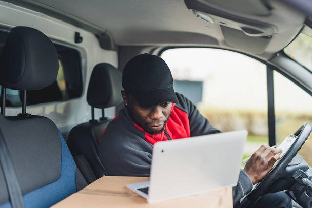 Medium closeup shot POV of passenger seat. Adult focused African-American man seating behind the wheel of white delivery truck checking address information about his next destination. High quality - Photo, Image
