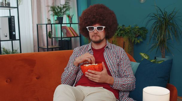 Muotokuva valkoihoinen innoissaan nuori mies istuu sohvalla syö popcornia ja katsella mielenkiintoisia tv-sarja, urheilupeli, elokuva, online sosiaalisen median elokuvan sisältöä kotona. Guy nauttii kotimaista viihdettä - Valokuva, kuva