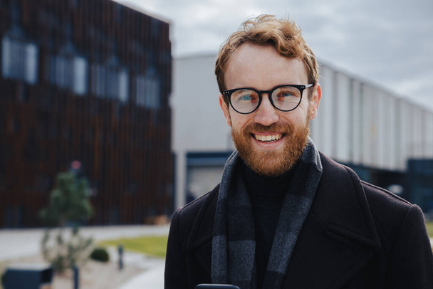 A young red-haired guy, a businessman in glasses, looks at the camera against the background of an urban style. Close up portrait. - Foto, immagini