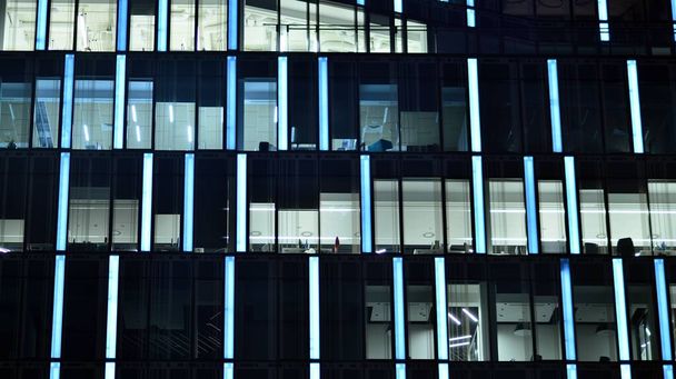 Moderní kancelářská budova ve městě v noci. Pohled na osvětlené kanceláře korporátní budovy. Blikající světlo v okně vícepodlažní budovy ze skla a oceli. Dlouhá expozice v noci - Fotografie, Obrázek