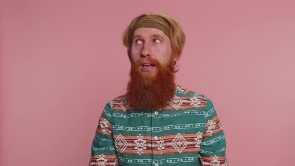 Funny joyful sincere redhead hippie man in pattern shirt making playful silly facial expressions and grimacing, fooling around showing tongue. Young handsome hipster guy isolated on pink background - Footage, Video