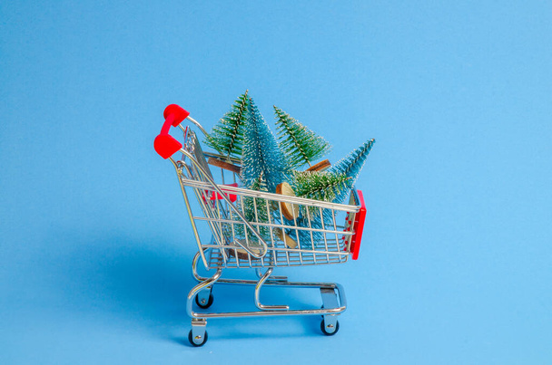 Carrito de compras en miniatura con pequeños árboles de Navidad artificiales en el interior. concepto de compras de Navidad - Foto, imagen