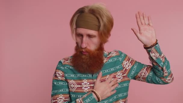 I swear to be honest. Sincere responsible hippie redhead bearded man raising hand to take oath, promising to be honest and to tell truth, keeping hand on chest. Hipster ginger guy on pink background - Footage, Video