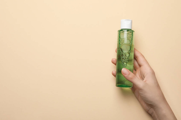 Woman holding micellar water in bottle on beige background, closeup. Space for text - Fotografie, Obrázek