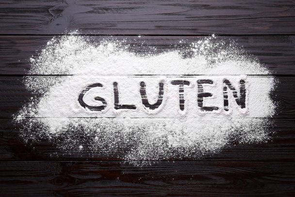 Word Gluten written with flour on brown wooden table, top view - Foto, Imagen