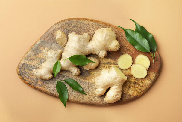 Fresh ginger with green leaves on light pale brown background, top view - Fotografie, Obrázek