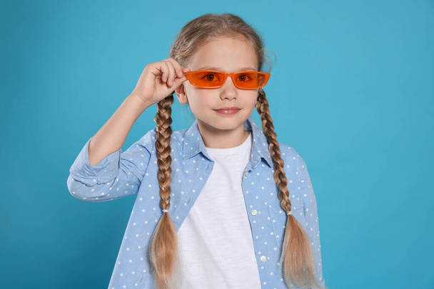 Girl in orange sunglasses on light blue background - Foto, imagen