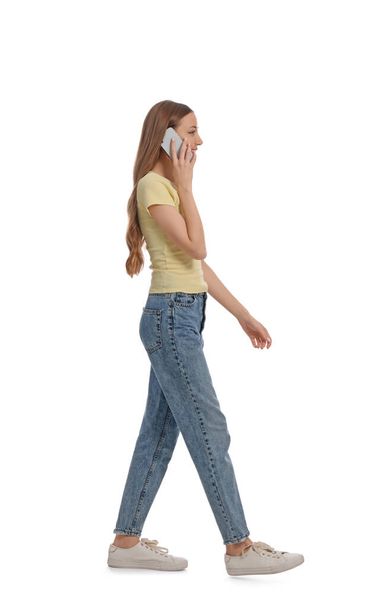 Young woman in casual outfit talking on smartphone while walking against white background - Foto, imagen