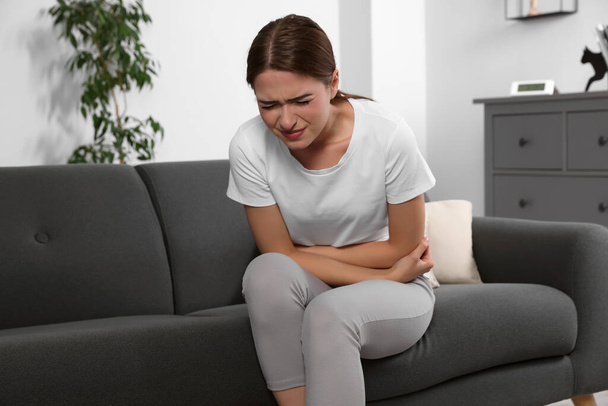 Young woman suffering from cystitis on sofa at home - Foto, immagini