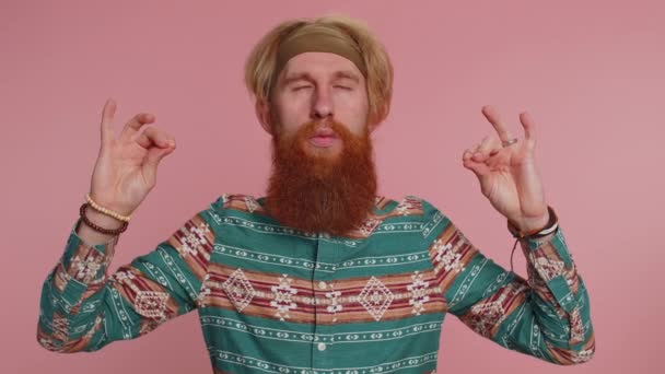 Keep calm down, relax, balance. Hippie redhead bearded man breathes deeply with mudra gesture, eyes closed, meditating with concentrated thoughts, peaceful mind. Hipster ginger guy on pink background - Footage, Video