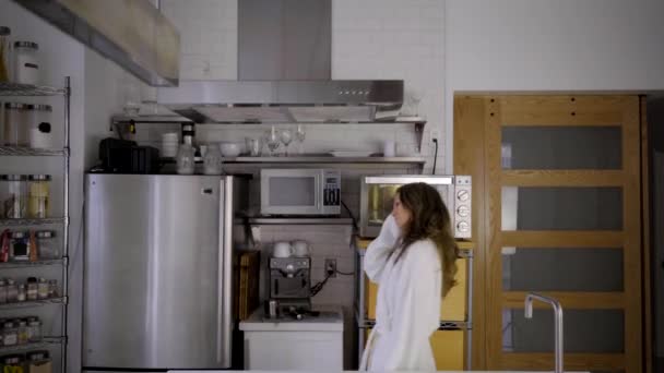 kaukázusi nő fehér fürdőköpenyben modern konyha almával - Felvétel, videó