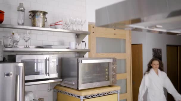 femme caucasienne en peignoir blanc dans la cuisine moderne avec pomme - Séquence, vidéo